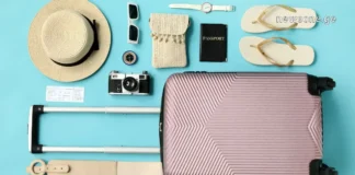 როგორ ჩავალაგოთ ჩემოდანი ისე, რომ ბევრი ნივთი ჩაგვეტიოს Flat lay of a pink travel suitcase with summer vacation essentials like a hat, passport, and camera on a blue background.