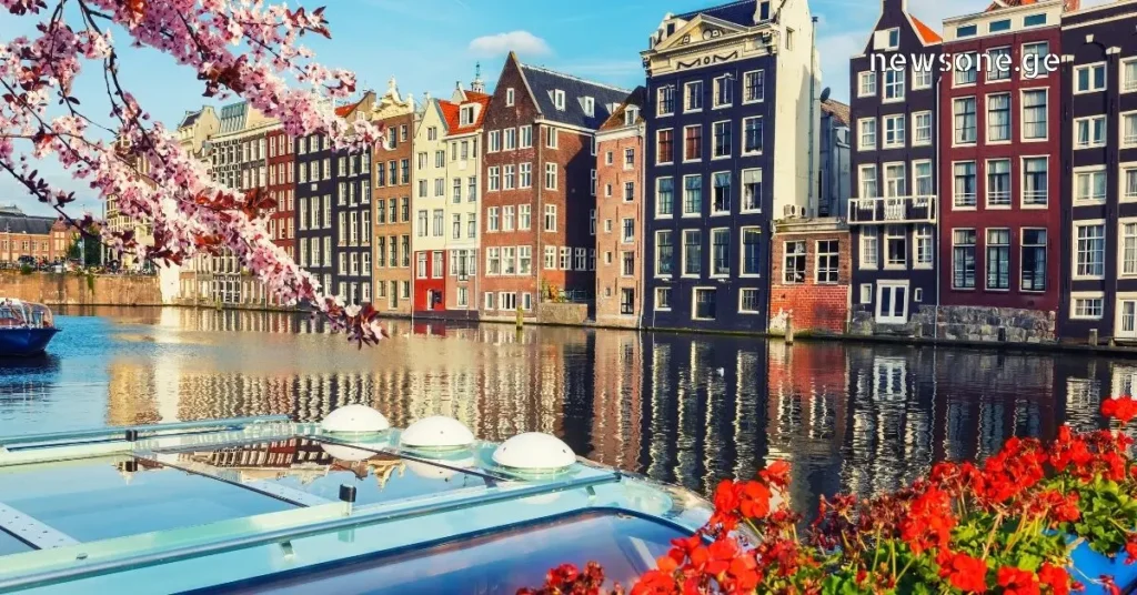Colorful traditional canal houses in Amsterdam with spring cherry blossoms and a boat in the foreground.