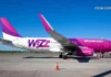 Wizz Air Georgia: სრული გზამკვლევი – როგორ ვიმოგზაუროთ ჭკვიანურად ქუთაისიდან A side profile view of a Wizz Air Airbus A320 aircraft with its white, purple, and magenta livery, parked on the airport tarmac under a clear blue sky.